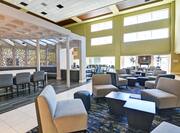 Lobby casual seating area with chairs, coffee tables, fireplace, and multiple large windows with sunlight shining in