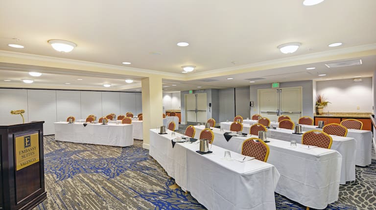 Meeting room with classroom setup, cloth-covered tables, chairs, and speaking podium