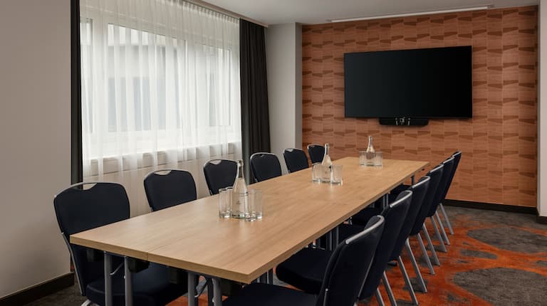 Pier 3 meeting room with a long table and chairs for 12 guests and a large wall-mounted screen.