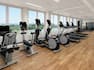 Fitness center exercise equipment facing floor-to-ceiling windows providing views of the outside.
