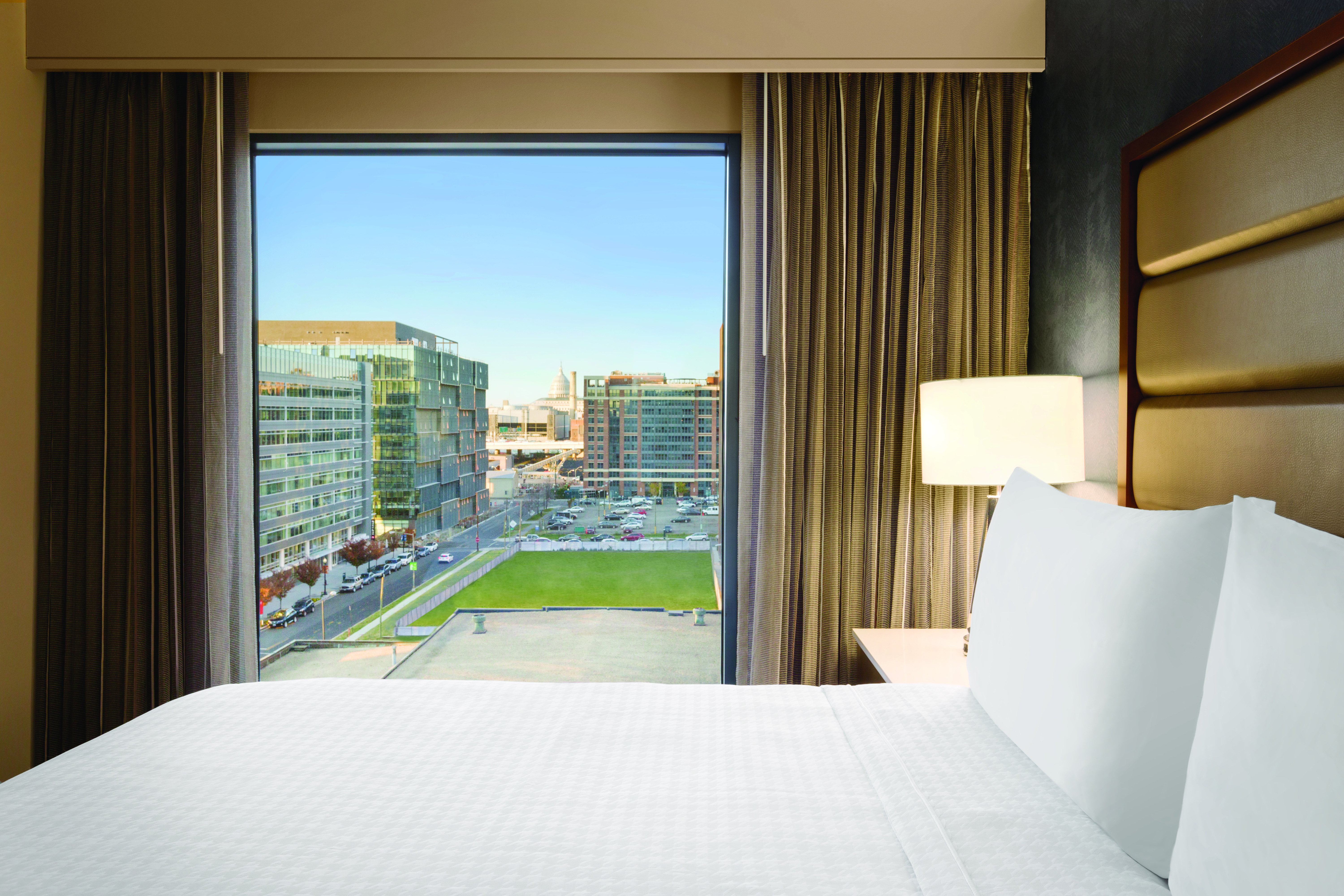 King Bed and Bedside Table with Lamp by Window with Open DrapesKing Mattress Beside a Window with Stunning City Views