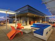 Table With Umbrella, Two Grills, Chairs, Tables, Blue Sofa on Roof Top Terrace Illuminated at NightRooftop Deck Featuring a Shared Seating Area, Grill and City Views