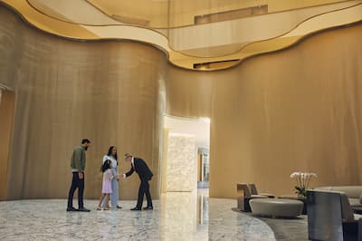 Un homme, une femme et un jeune enfant sont accueillis par un membre du personnel dans l'atrium