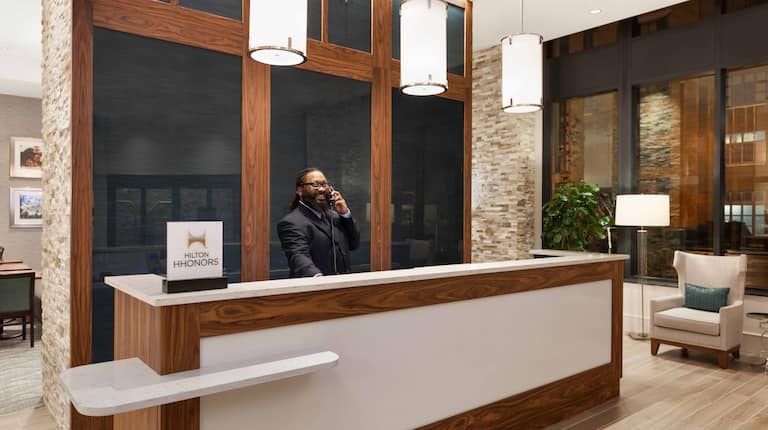 Diagonal View of Smiling Male Staff Member Behind Front Desk and Lobby Seating