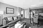  Suite Living Room With Sofa, Ottoman, Wall Art, Lamps, Open Doorway to Bathroom, Entry, Kitchen, and Dining Table