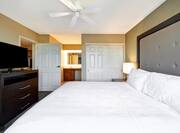 TV, Open Doorway to Kitchen, Ceiling Fan, Opening to Brightly Lit Vanity and Sink, Bedside Table With Lamp by King Bed