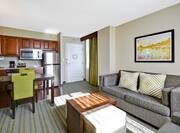 Suite Living Room Entry by Window, Wall Art, Sofa, Ottoman/Table Combo, Dining Table With Seating for Two, and Kitchen 