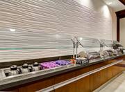 Angled View of Breakfast Buffet With Milk, Yogurt, Condiments, Hot Food Selections and Utensils