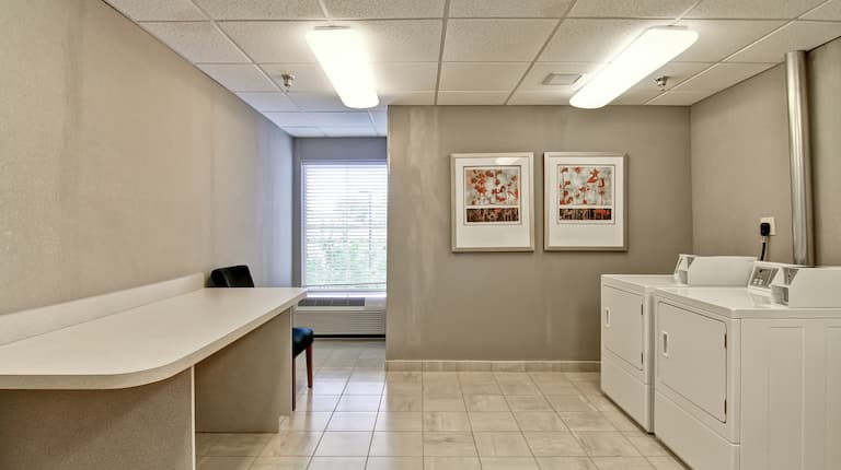Laundry Facilities With Folding Table, Chair, Window, Wall Art, Washer and Dryer