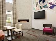 Lobby seating area with soft chairs, small tables, TV, fireplace, and window with outdoor view