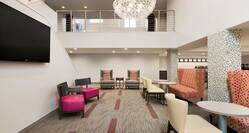 Lobby atrium seating area with soft chairs, lavish sofas, small tables, TV, and view of second floor banister