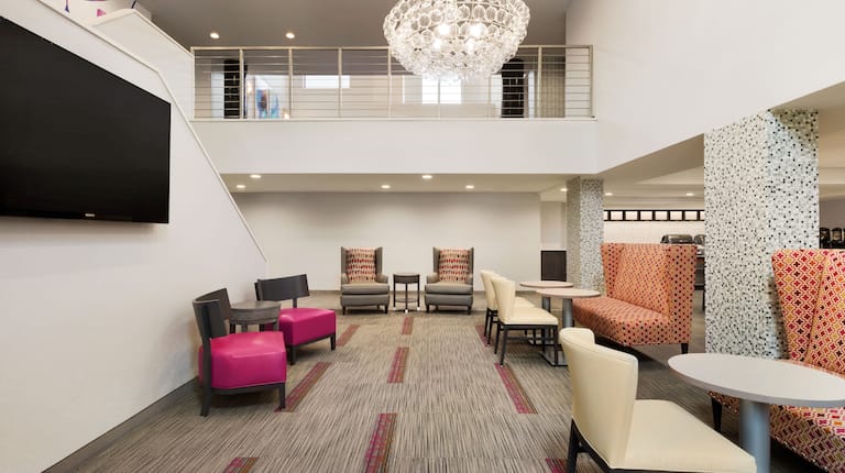 Lobby atrium seating area with soft chairs, lavish sofas, small tables, TV, and view of second floor banister