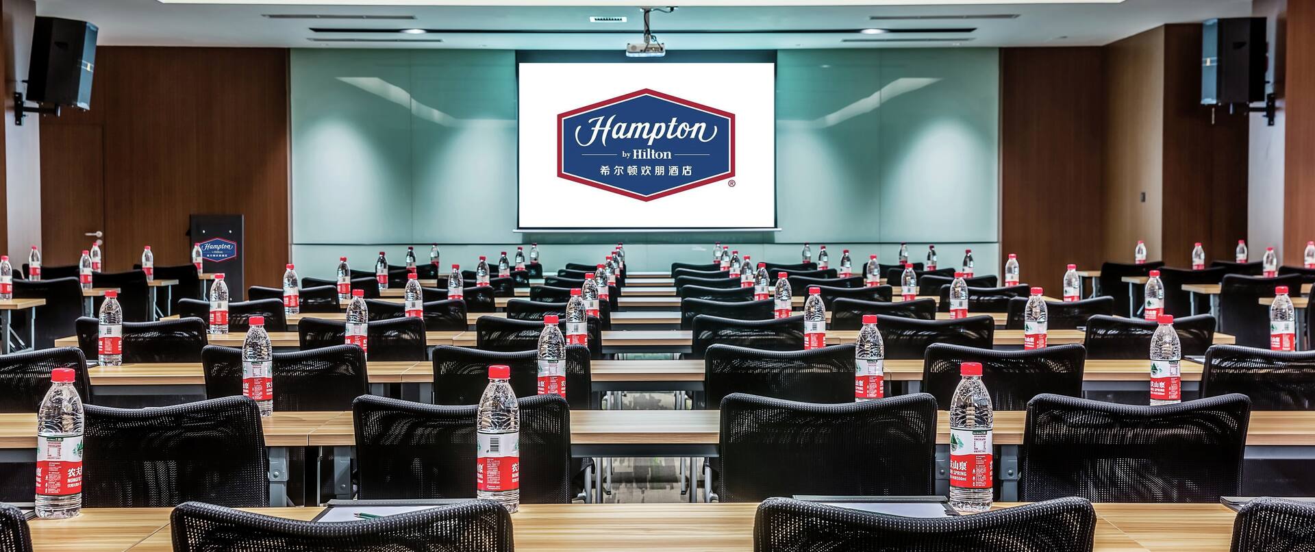 Large meeting room, rows of tables, chairs, large screen