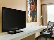 TV, Wall Art, and Desk With Ergonomic Chair by Window With Open Drapes