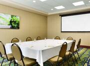 Wall Art, Presentation Screen, and Seating for 10 at Table With White Linens, Chairs, Drinking Glasses, and Notepads in Walden Meeting Room