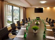 Boardroom With Window, TV, and Black Chairs Around a Long Table With Green Bottles of Water and Notepads