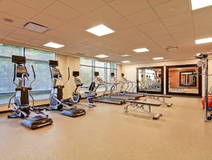 Fitness Room With Cardio Equipment Facing Large Windows, Weight Benches, Two Large Mirrors, Red Exercise Ball, and Weight Machine
