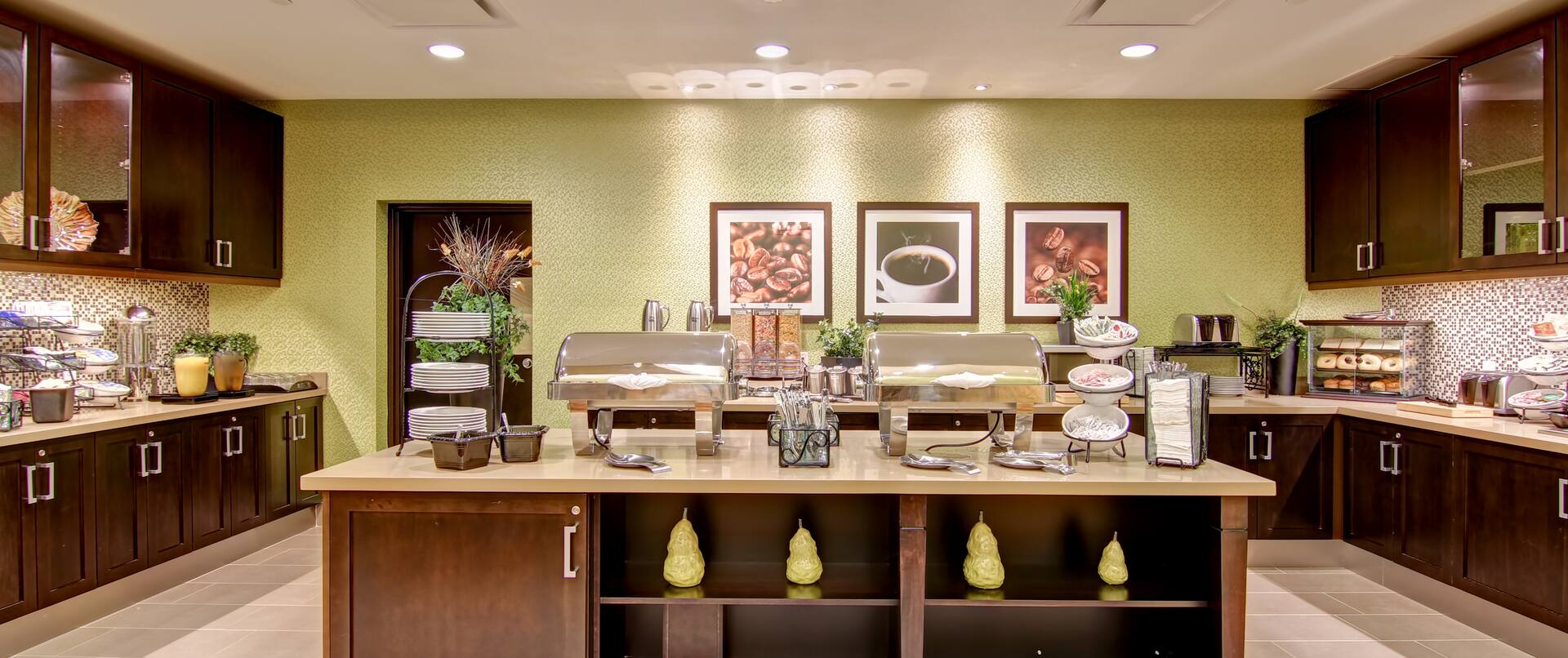 Plates, Utensils, Food, and Condiments on Counters of Hotel Dining Area With Wood Cabinets and Wall Art