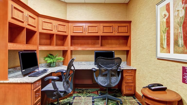 Centre d'affaires avec placards en bois, deux postes de travail avec ordinateur et chaise ergonomique