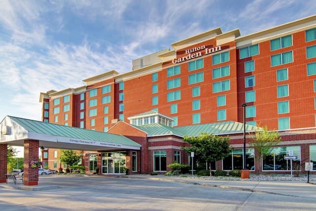 Daytime View of Hotel Exterior With Signage, Porte Cochère, Entrance, and Guest Cars on Parking Lot