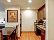 Accessible Kitchen With Fridge, Microwave, Dishwasher, Sink, Wall Art Above Dining Table and Open Doorway to Bedroom