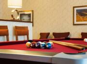 Detailed View of Cue Sticks and Balls on a Pool Table With Chairs and Wall Art in Background of Game Area