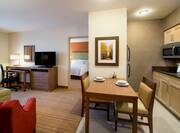 Kitchen, Wall Art Above Dining Area, Living Area Seating, Work Desk, TV, and Open Door to Bedroom in Queen Suite