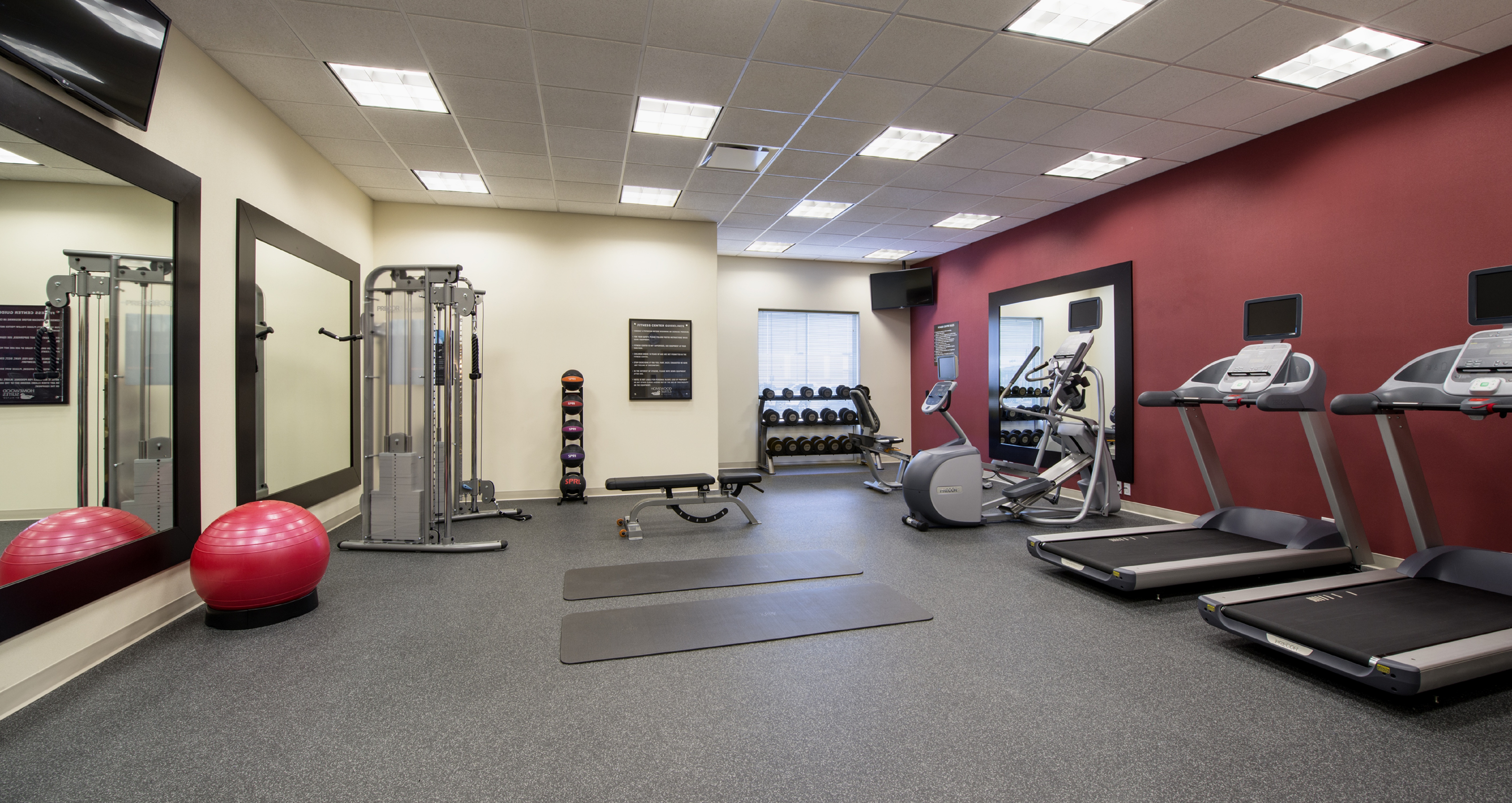  Fitness Center With Cardio Equipment, TV Above Large Mirrors, Red Exercise Ball, Weight Machine, Weight Balls, Weight  Bench, and TV Above Free Weights