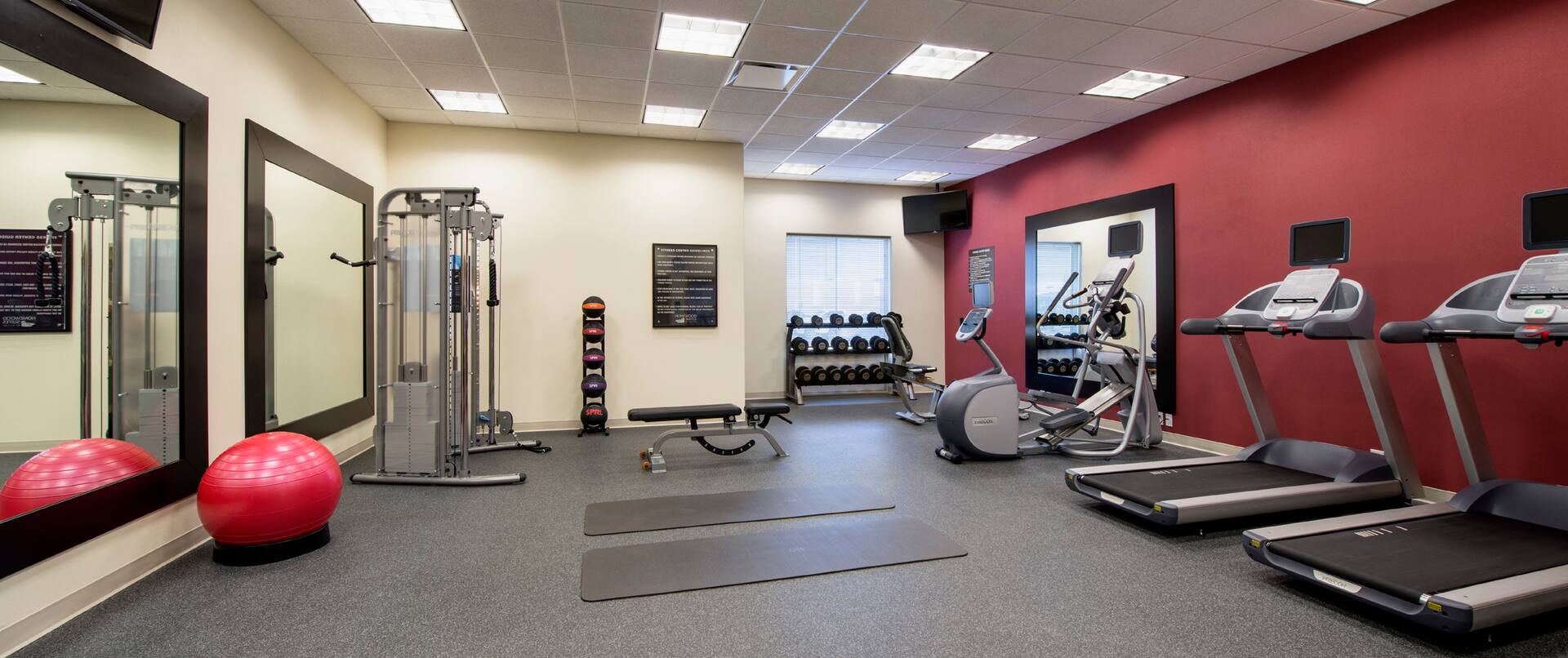  Fitness Center With Cardio Equipment, TV Above Large Mirrors, Red Exercise Ball, Weight Machine, Weight Balls, Weight  Bench, and TV Above Free Weights