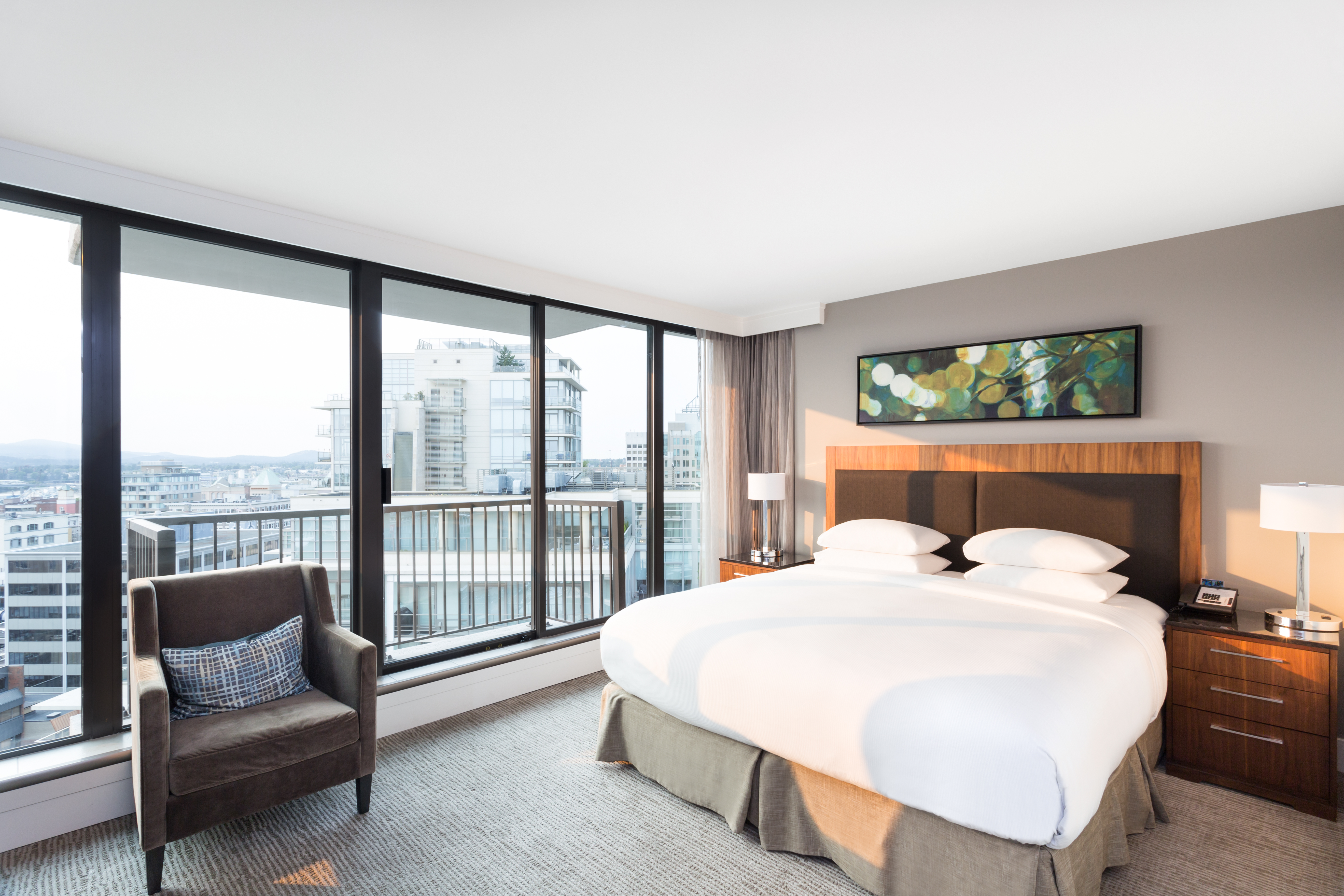 King-Sized Bed with Bed Tables, aChair by Window, and a Balcony That Overlooks the City in a Standard Guest Room