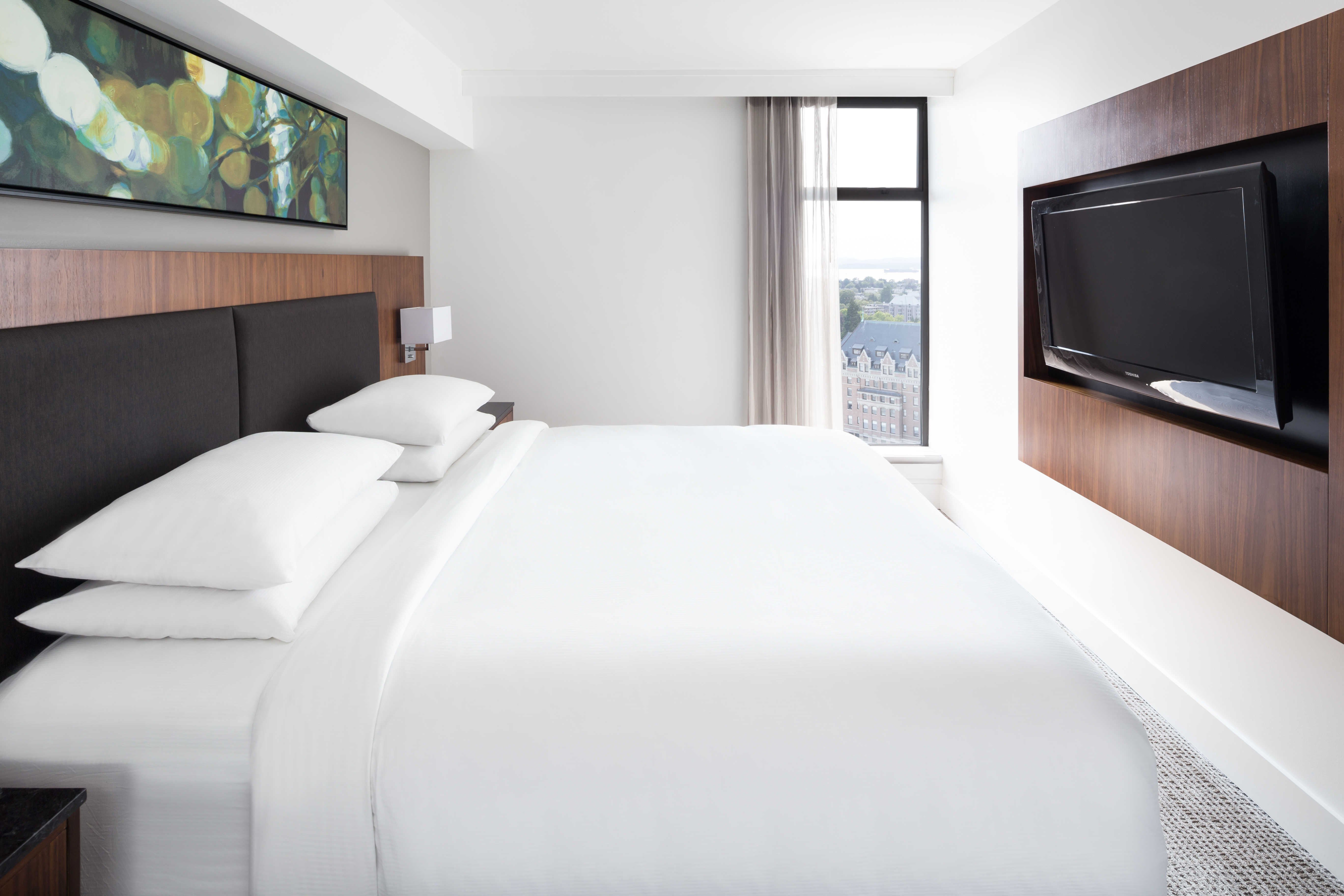 King-Sized Bed, Artwork, Open Curtains with a View of Outside, and Mounted TV in Suite Bedroom