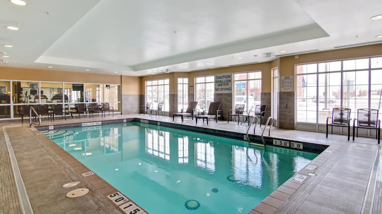  Daytime View of Indoor Pool With Tables, Chairs, Loungers, and Windows With Views of Fitness Center and Outside