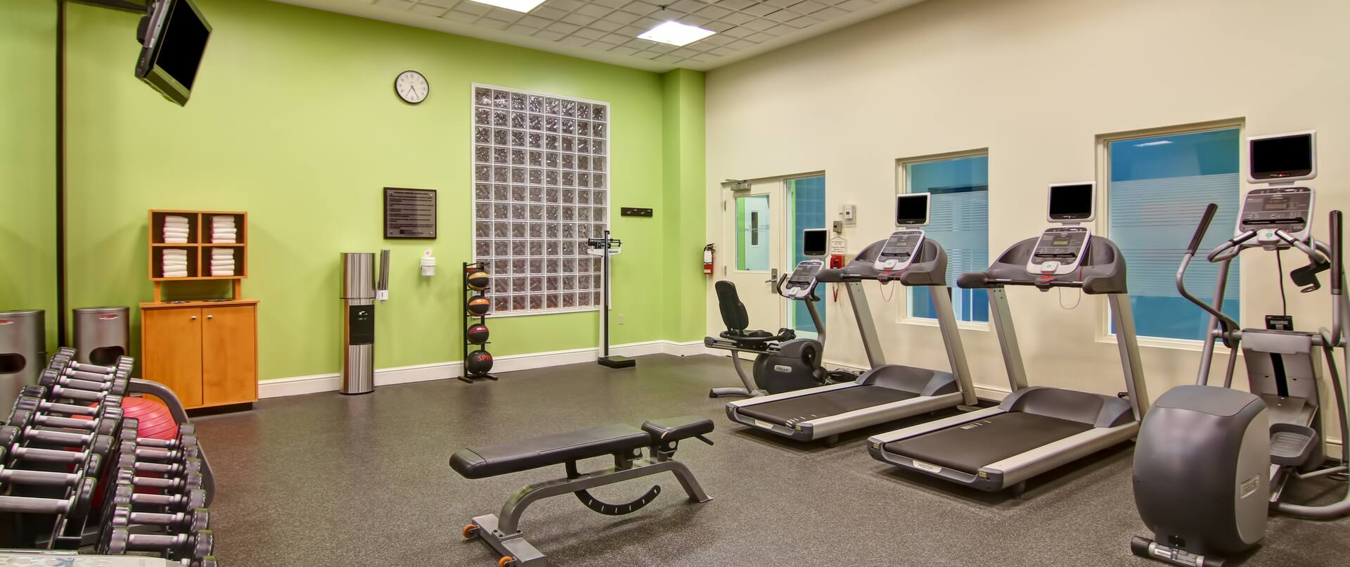 Fitness Center With Towel Station, Water Cooler, Weight Balls, Scale, Bench, Cardio Equipment, TVs Above Free Weights, and Red Stability Ball