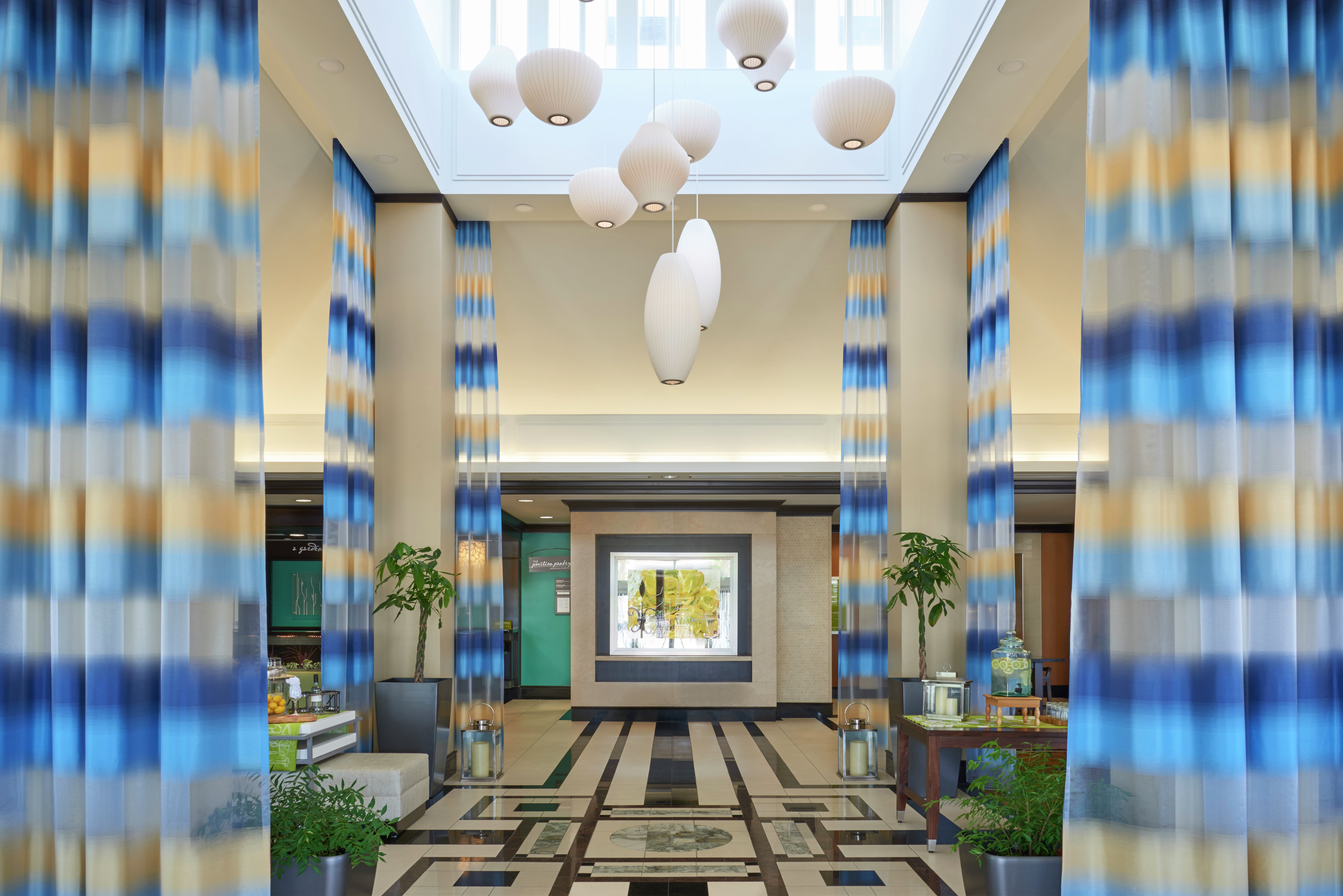 Two Beverage Service Tables in Vast Lobby With Long Drapes, Decorative Lighting, Lounge Seating and Art Feature