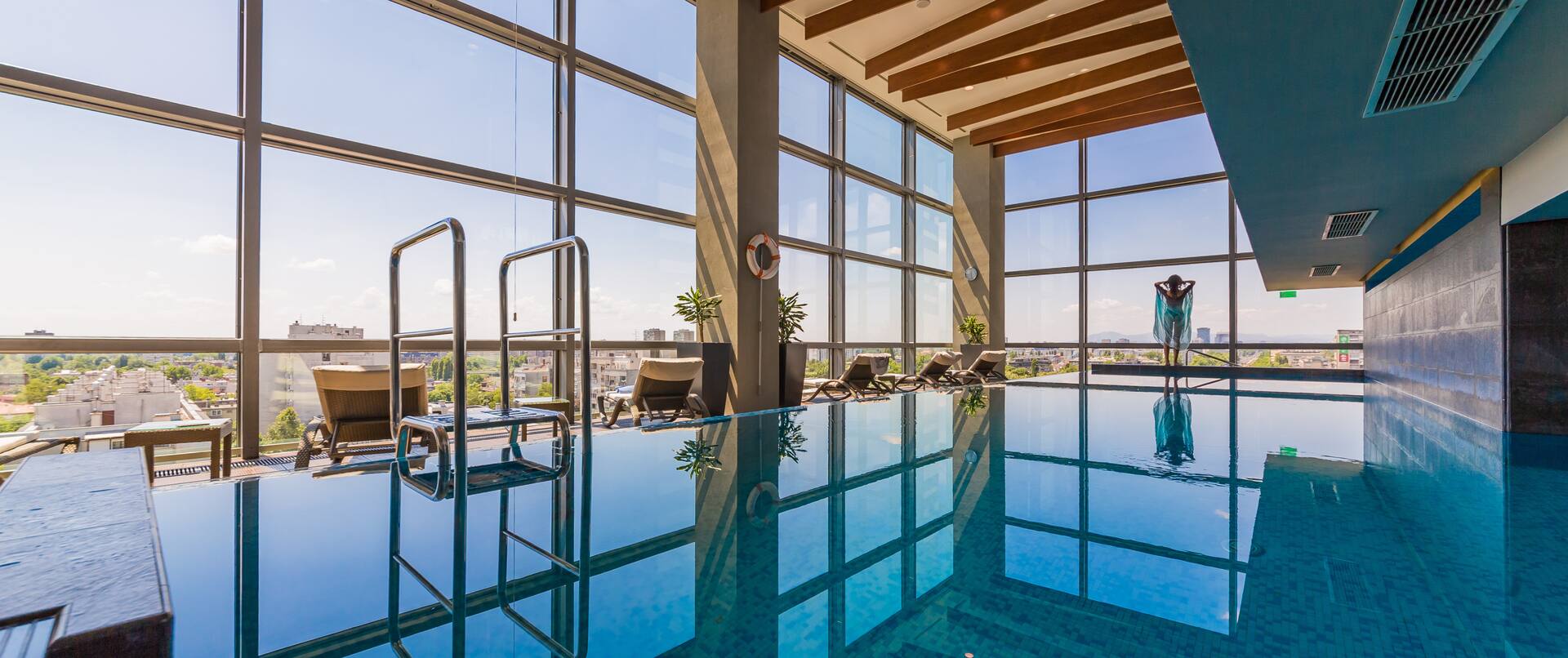 Indoor swimming pool with floor to ceiling windows and views of the city and outdoors